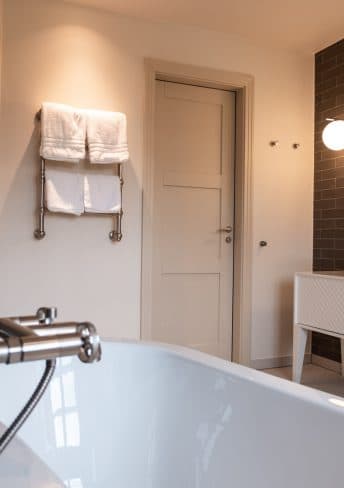Freistehende Badewanne mit Handtuchhalter und dunkler Fliesenwand