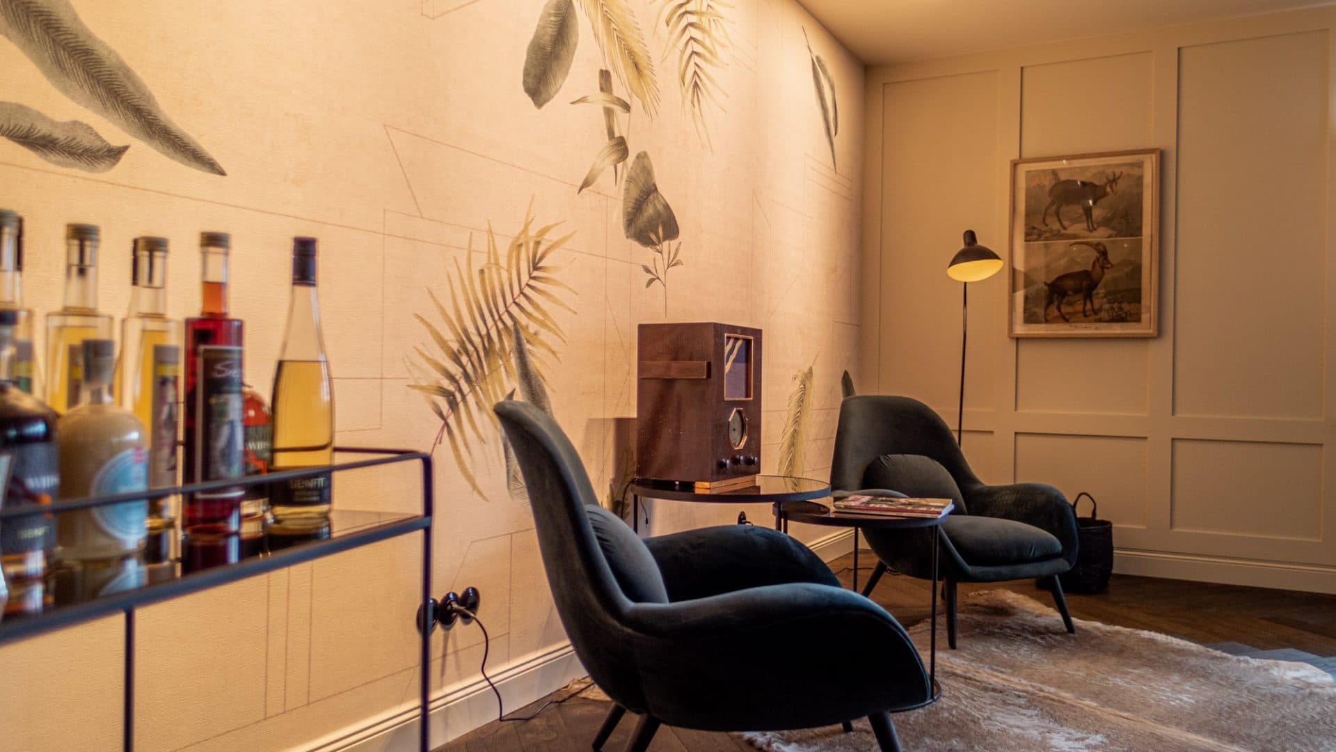 Lounge der Alpenloge mit Barwagen, botanischer Tapete und dunkelgrünen Sesseln