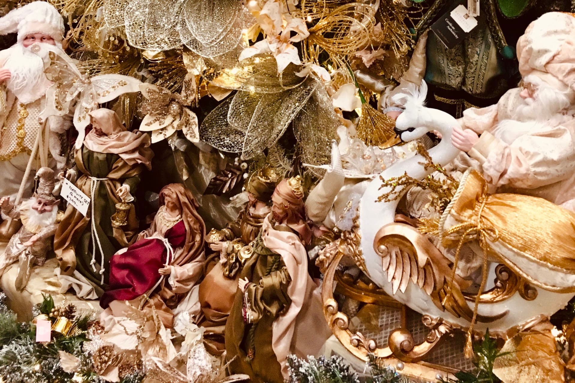 Weihnachtsschmuck in Gold und Creme: Krippenfiguren, ein Weihnachtsmann im weißen Schwanenschlitten und glitzernde Blüten