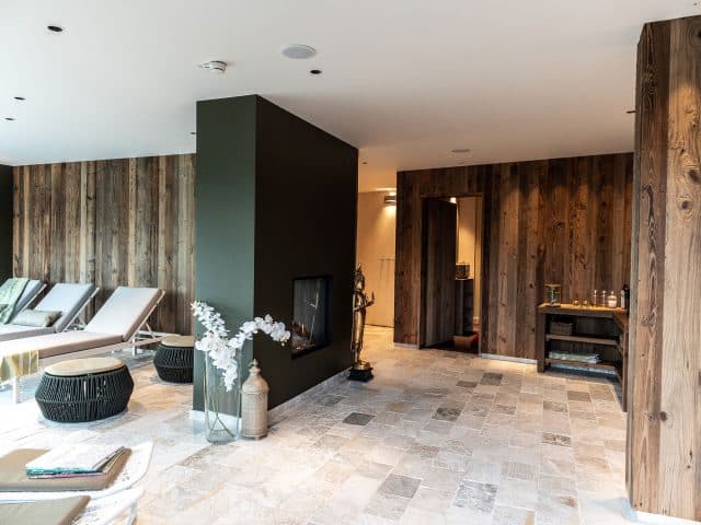 Relaxation room with loungers, fireplace and natural stone floor, a shelf with glasses to the right