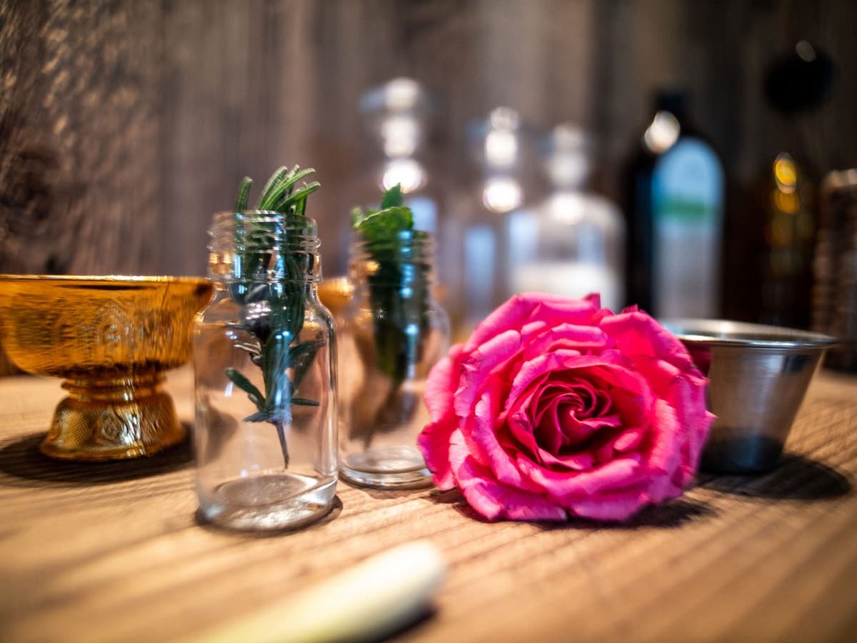 Ölfläschchen mit Rosmarinzweigen, eine Rose und eine Messingschale auf einem Holztisch
