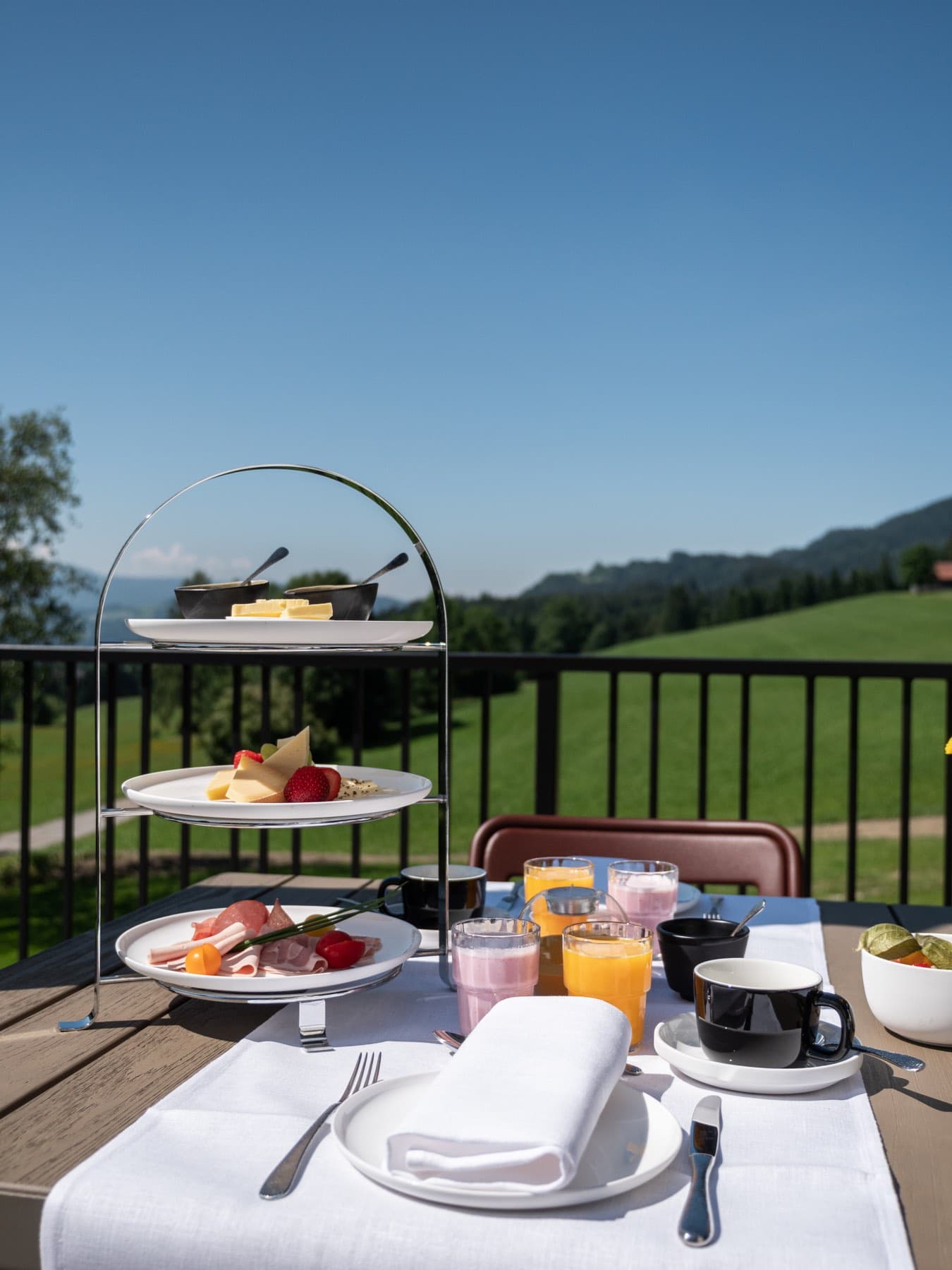 Dreistöckige Etagere auf dem Terrassentisch, dahinter Wiesen und blauer Himmel