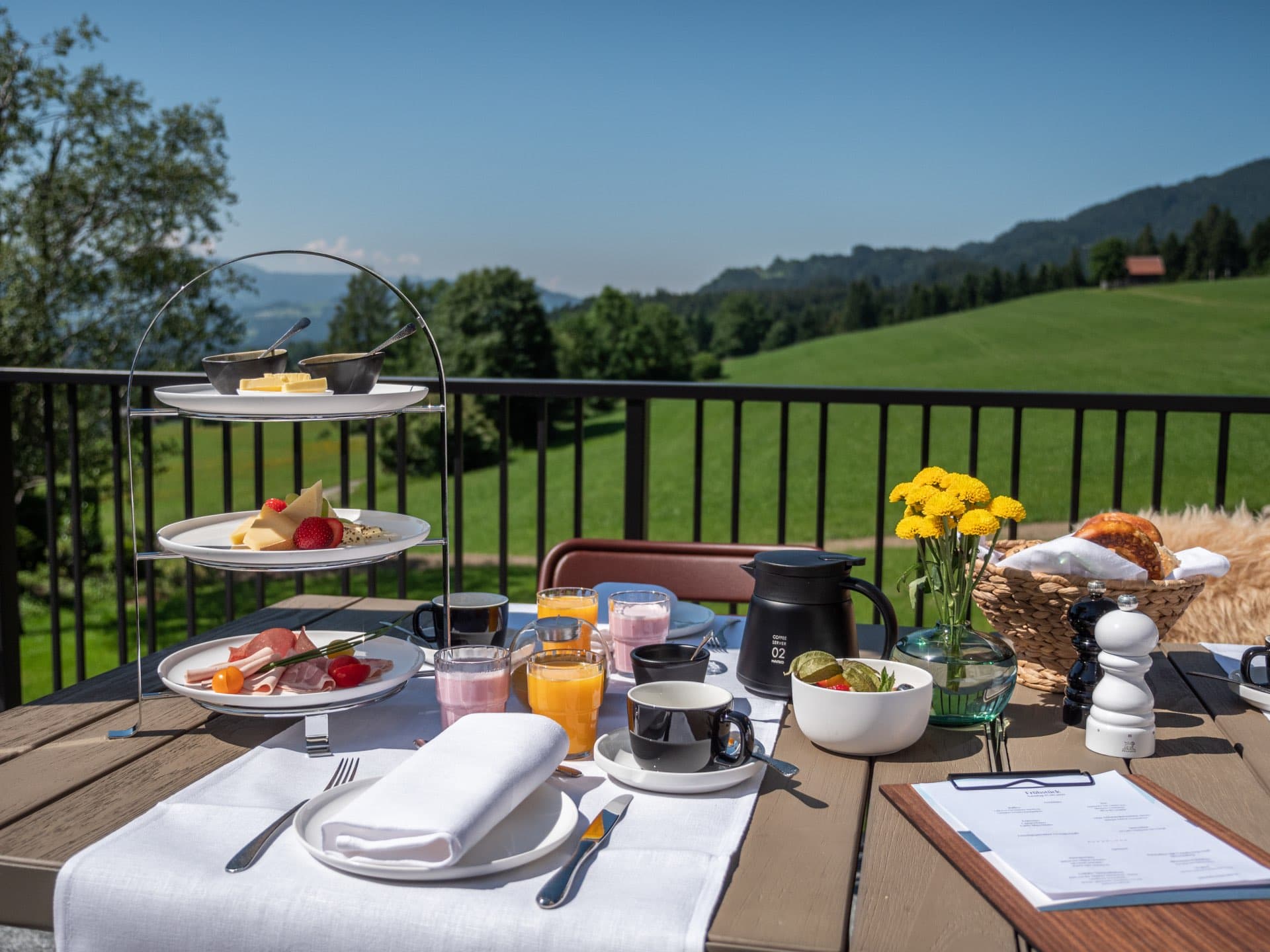 Gedeckter Frühstückstisch auf der Terrasse mit Etagere, Kaffeekanne und Blick über die Wiesen