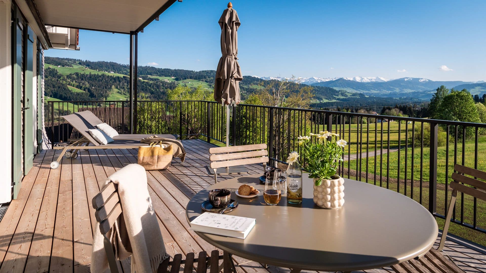 Terrasse der Suite Drei mit Sonnenliegen und Blick über die Wiesen bis ins verschneite Alpenpanorama