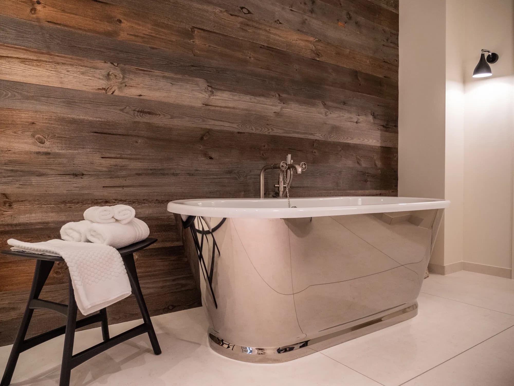 Freestanding bathtub against reclaimed wood, towels on a black stool