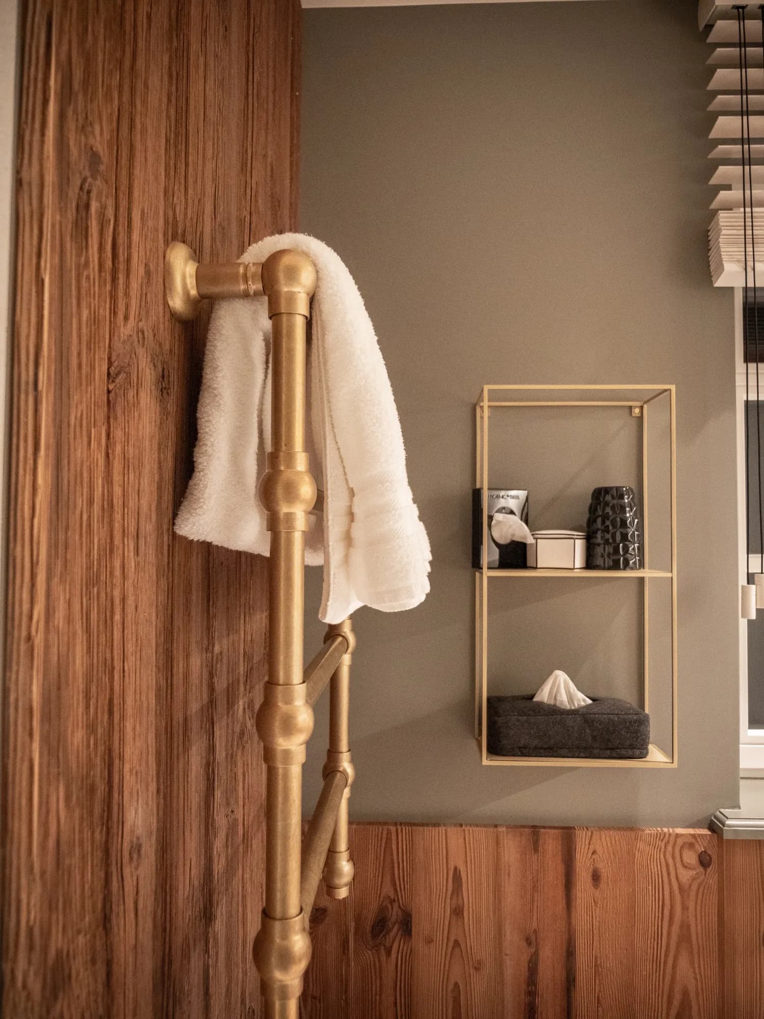 Brass towel rail against reclaimed wood, an open wall shelf with amenities beside it