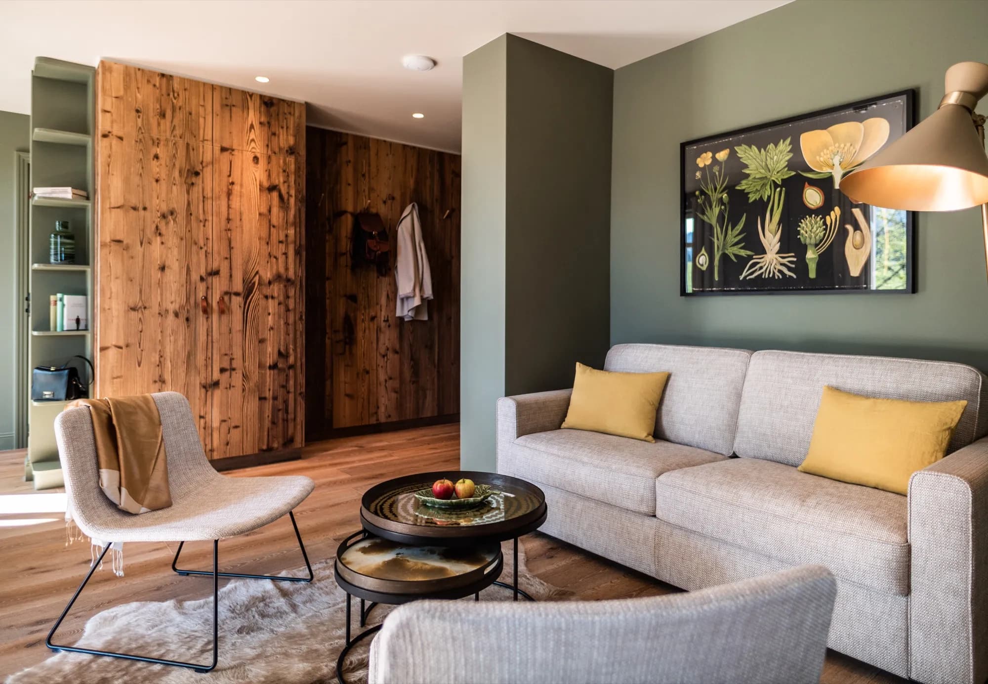 Seating area of Suite Three with a light sofa against a green wall, reclaimed wood to the left, a botanical print above