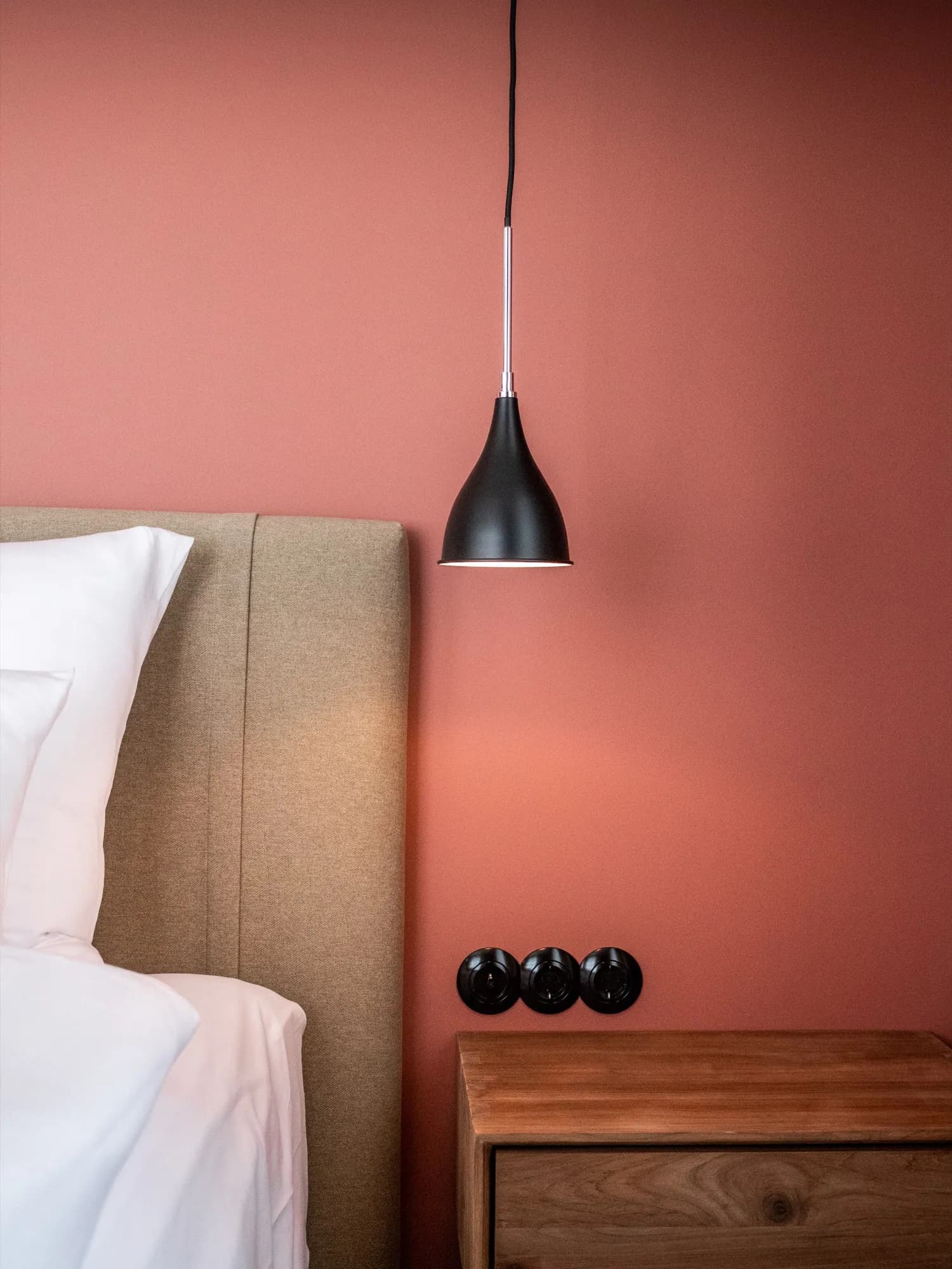 Schwarze Pendelleuchte über dem Nachttisch vor rosafarbener Wand
