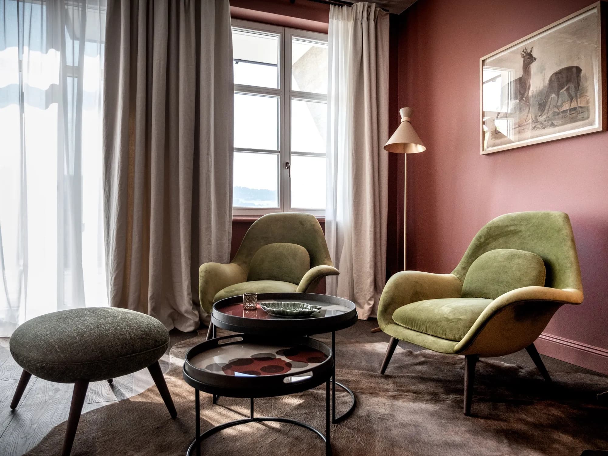 Sitzecke der Suite Eins mit olivgrünen Sesseln vor rosafarbener Wand, Beistelltische aus dunklem Metall
