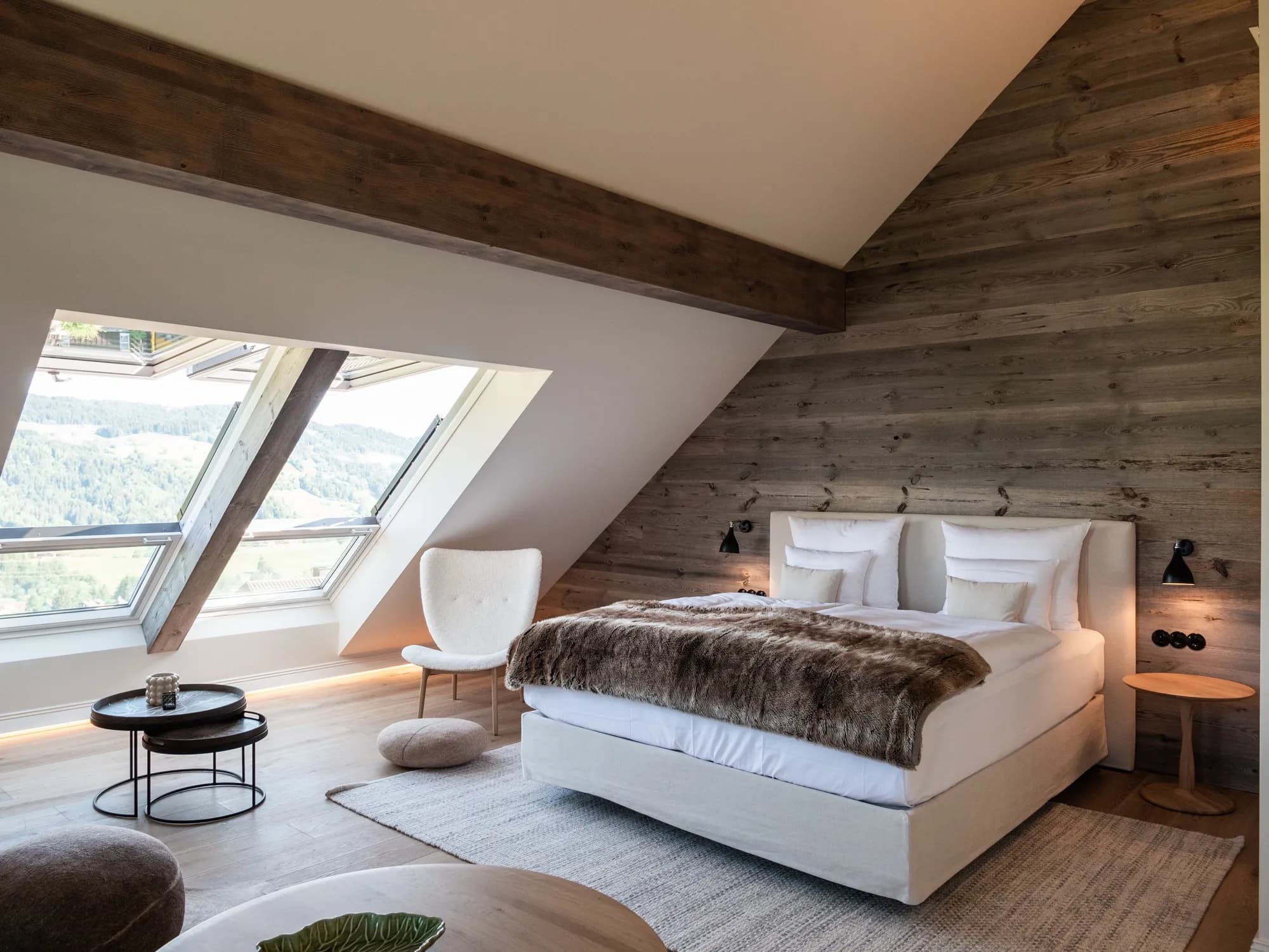 Overview of Suite Nine with the bed against the reclaimed-wood wall, roof beam and an open dormer window with a view