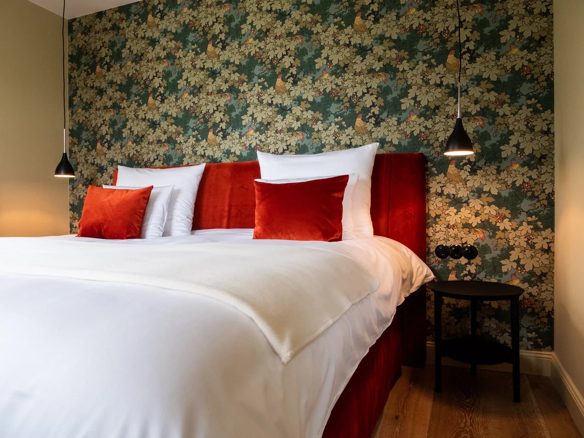 Bett der Suite Sechs vor Weinreben-Tapete in Grüntönen, Kopfteil und Kissen in Rot