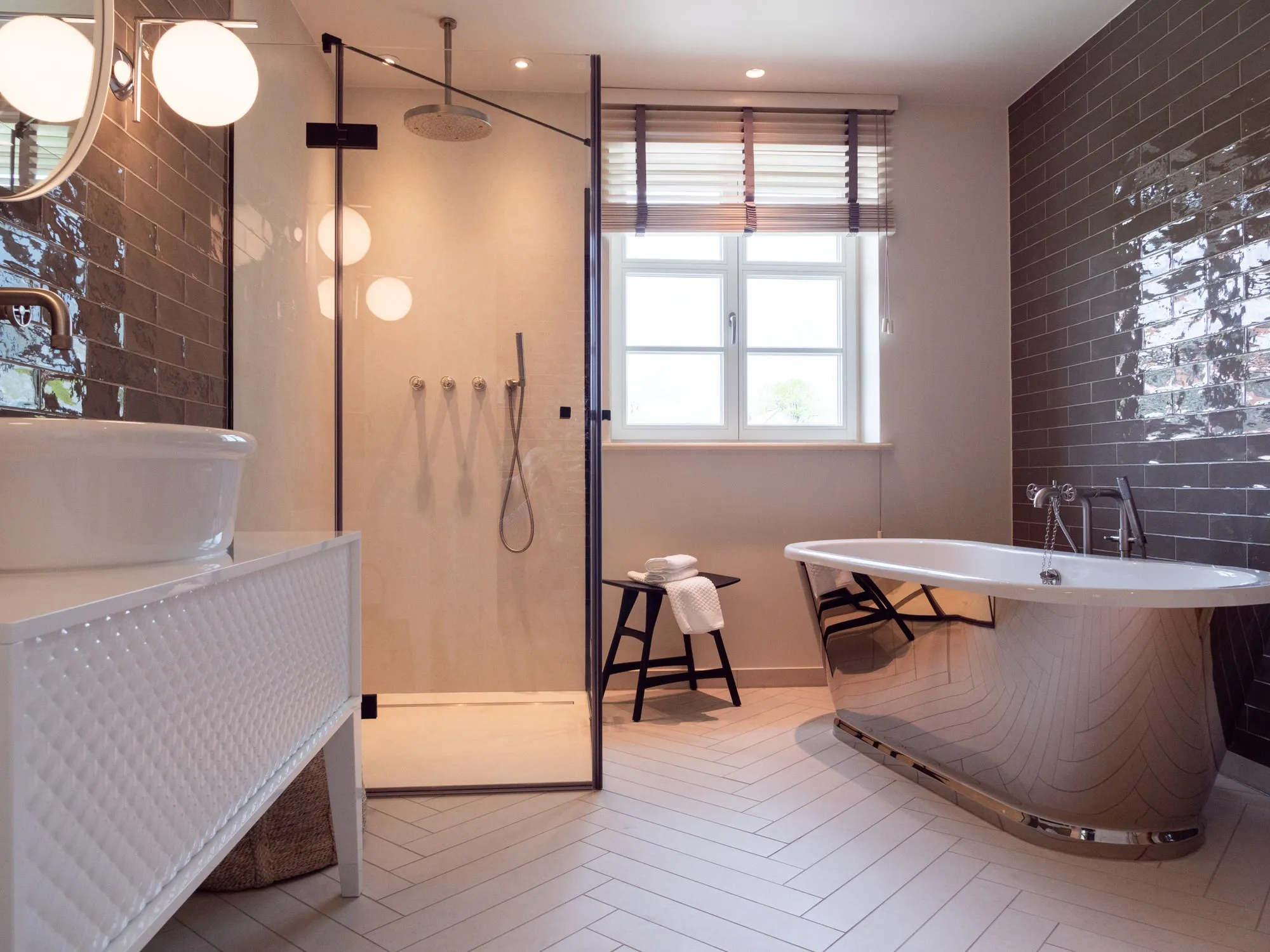 Freistehende Badewanne vor der Wand mit Weinreben-Tapete, Handtücher auf einem Hocker