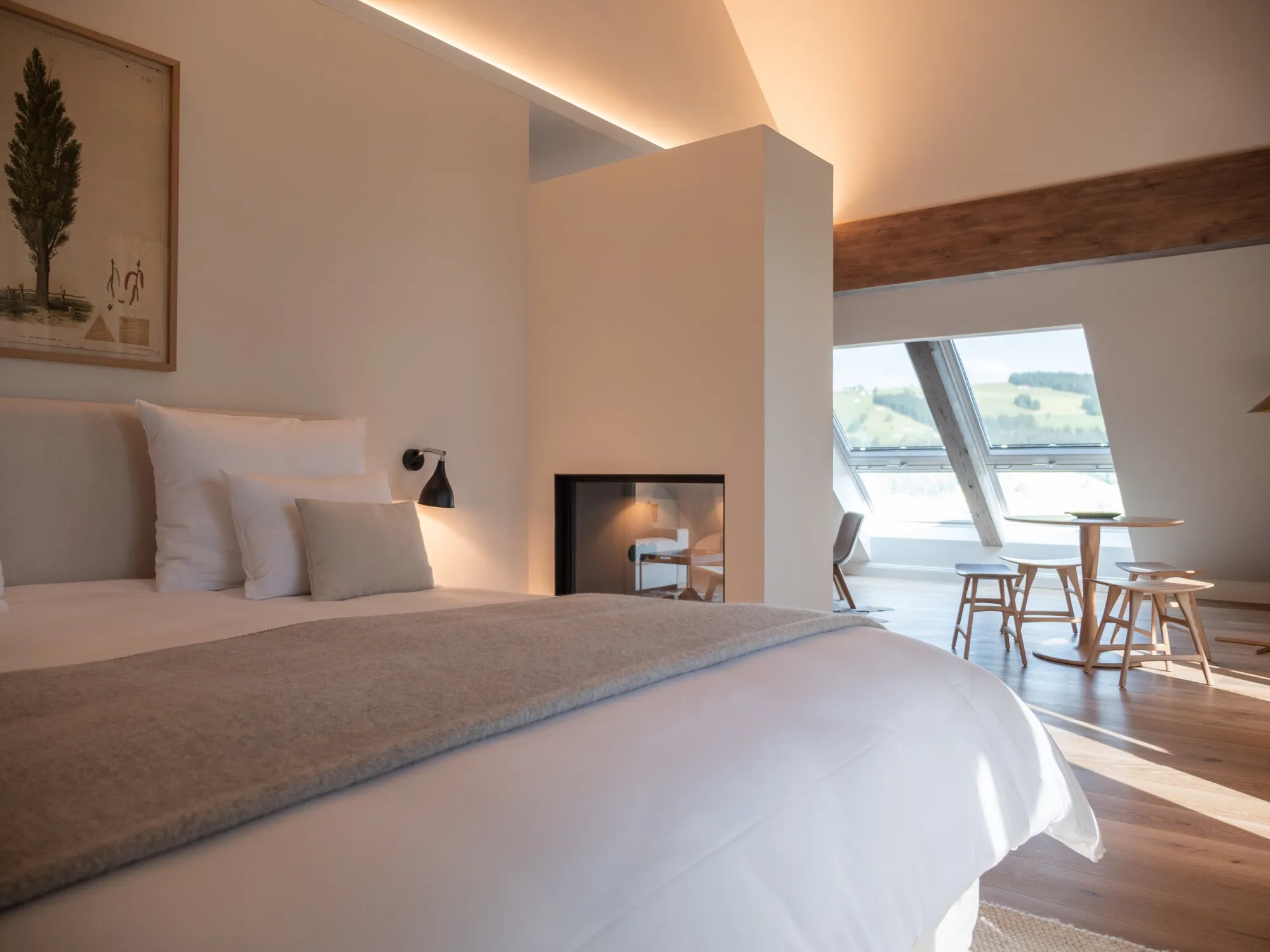 Bett der Suite Sieben mit Blick zum Gaskamin, dahinter der Tisch am Fenster mit Alpenblick