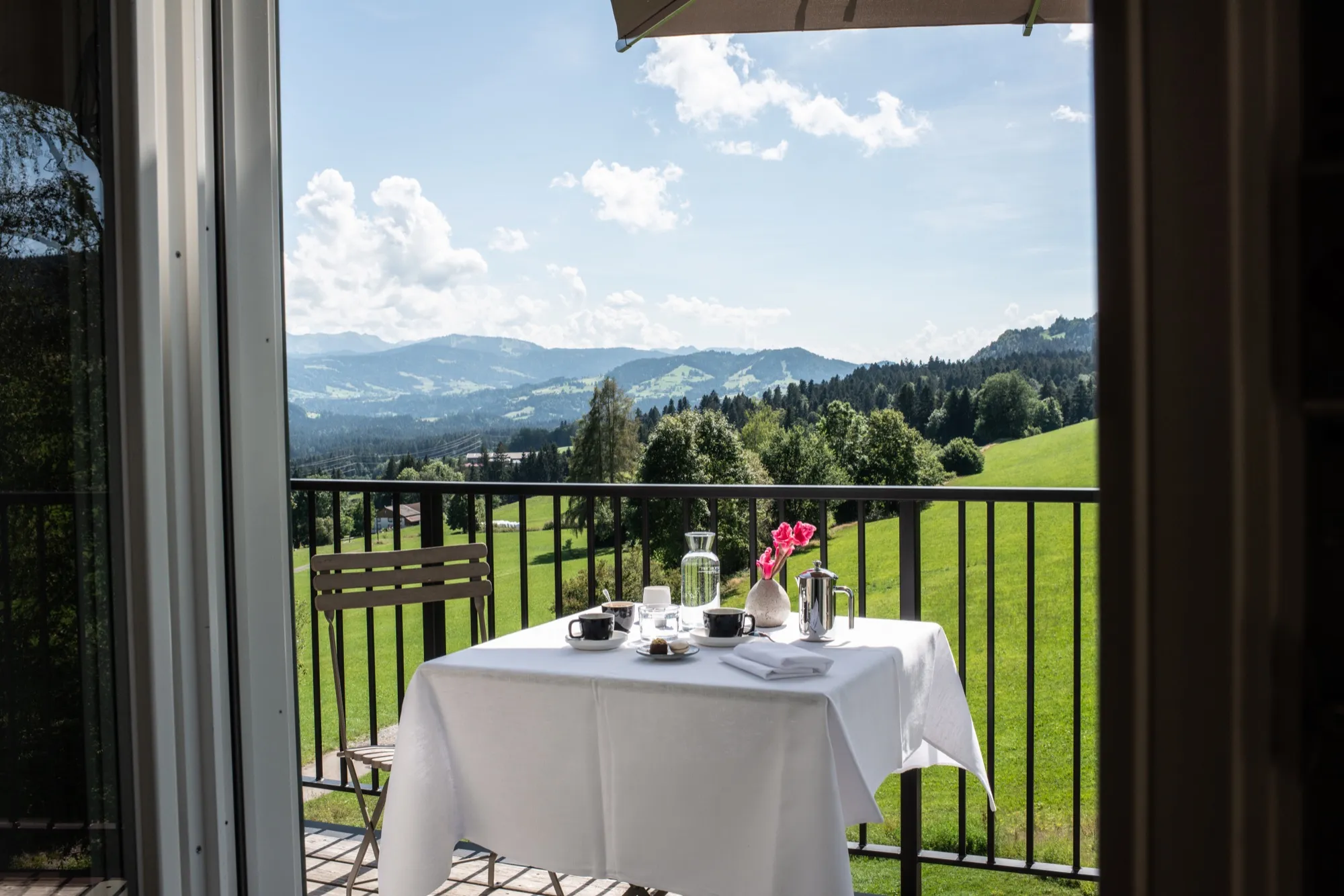 Gedeckter Tisch auf dem Balkon der Suite Sieben, Blick über Wiesen bis zu den Alpen