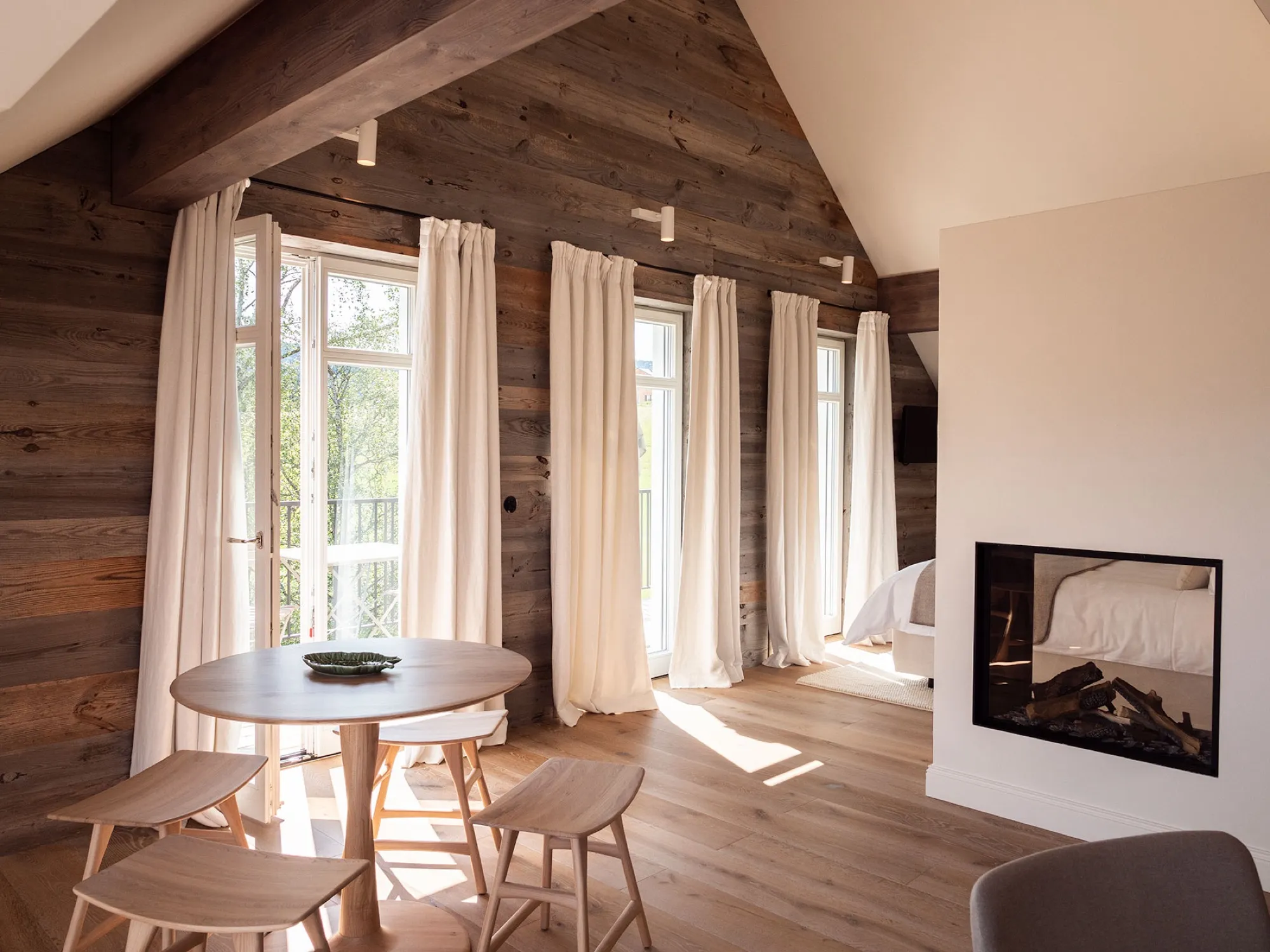 Dining area of Suite Seven under the roof, round table and chairs against reclaimed wood and curtains