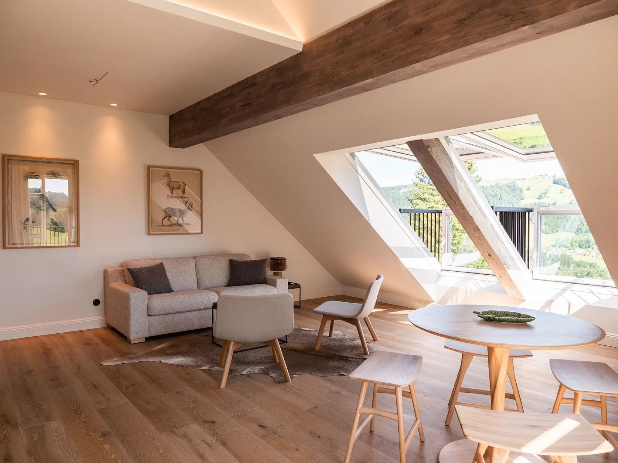 Sitzecke der Suite Sieben unterm Dachbalken, Sofa und runder Tisch mit Stühlen vor dem Panoramafenster