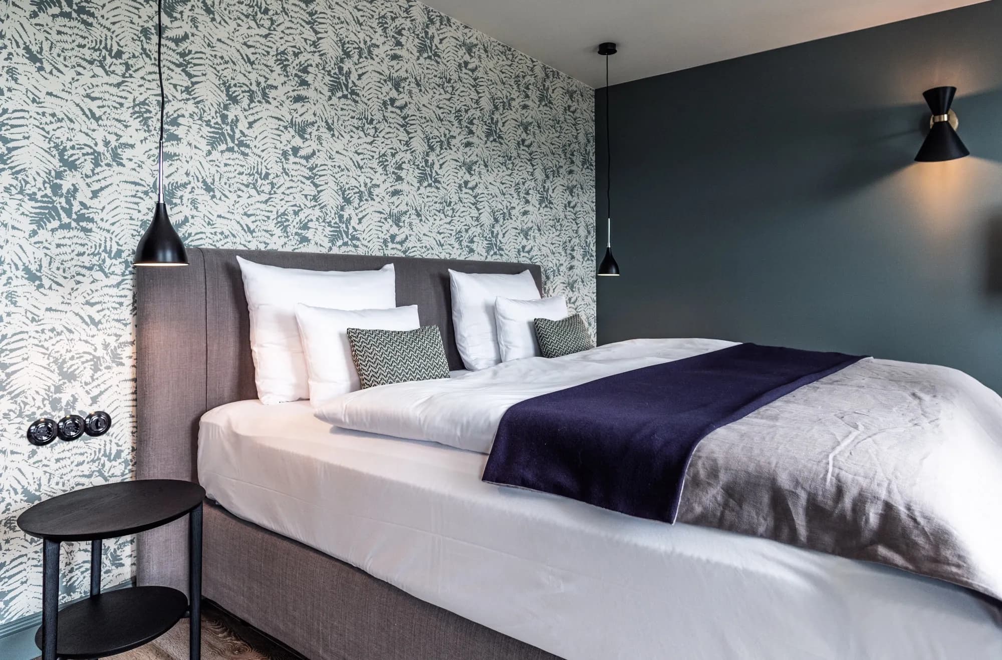 Bläuliche Tapete mit Farnmotiven an der Wand der Suite Vier, Bett mit hellem Kopfteil