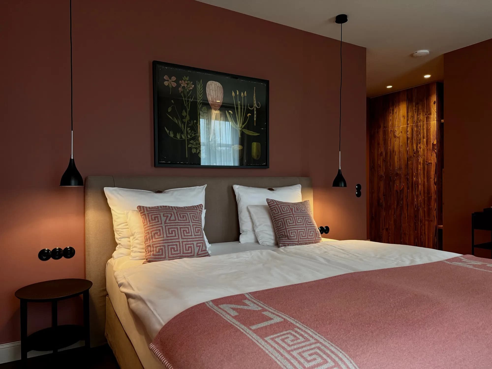 Bett der Suite Zwei vor terrakottafarbener Wand, darüber ein botanisches Bild, rechts der Altholzschrank